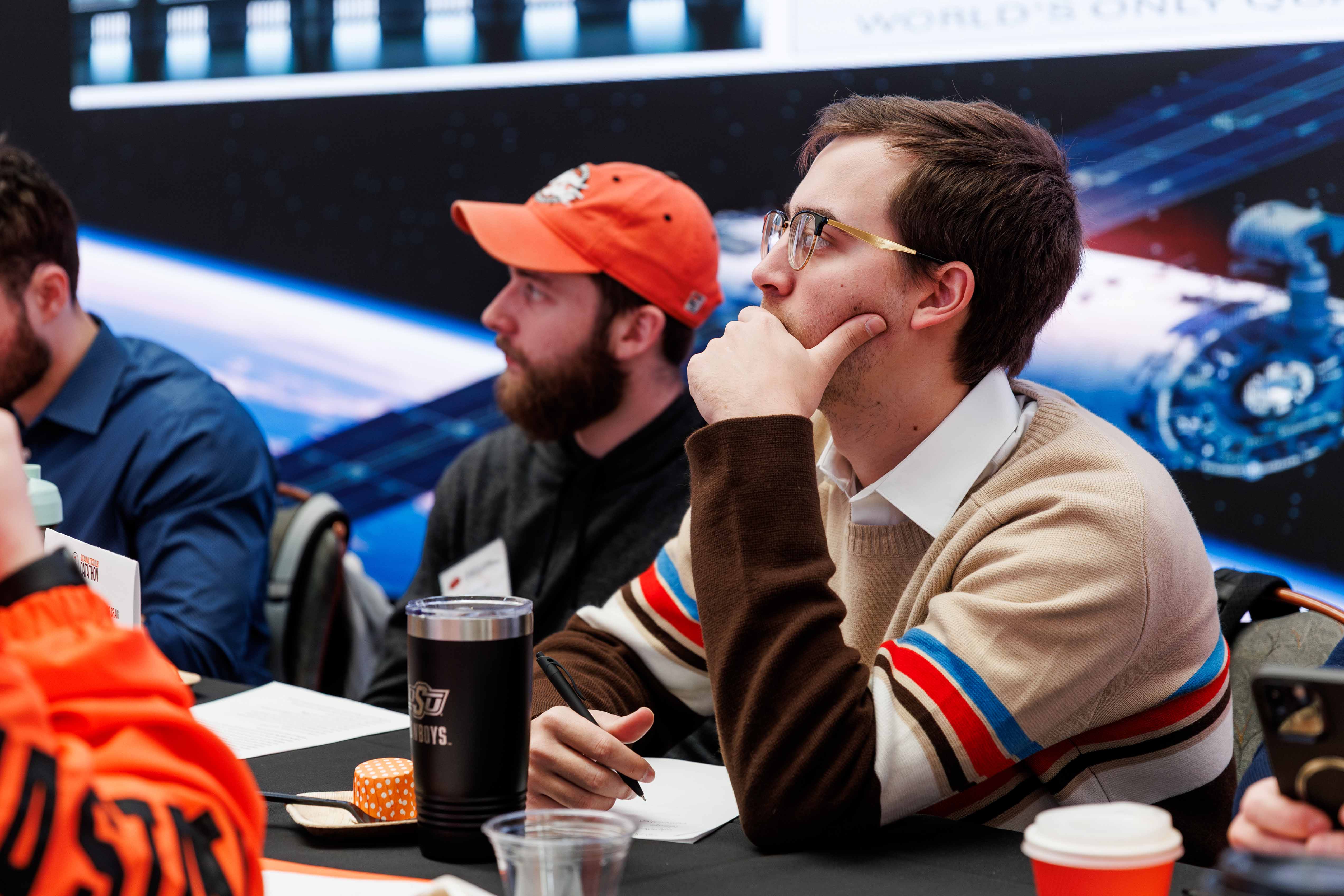 Male student looking intently resting his chin on his hand with a pen in hand.