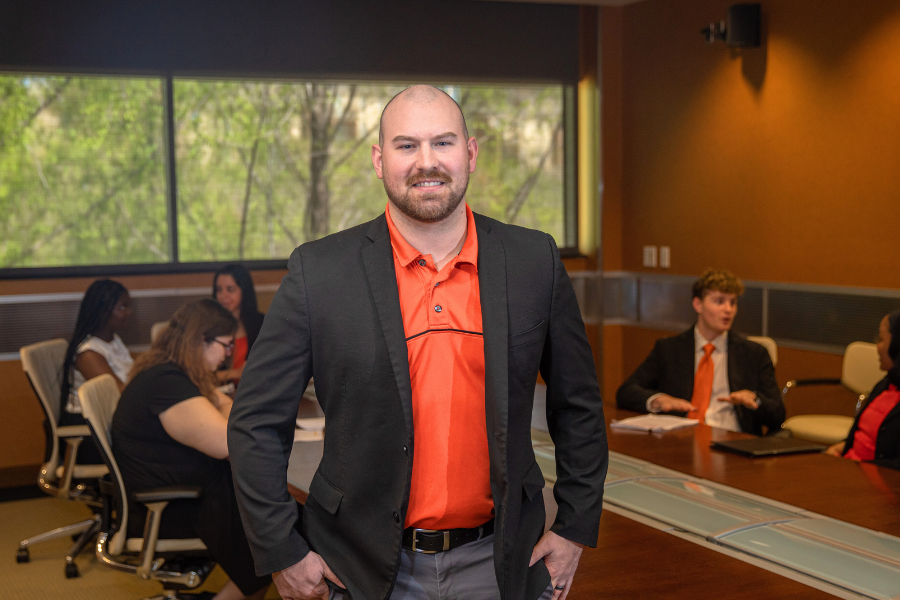 Professionals in conference room as man in orange shirt stands in front of the table