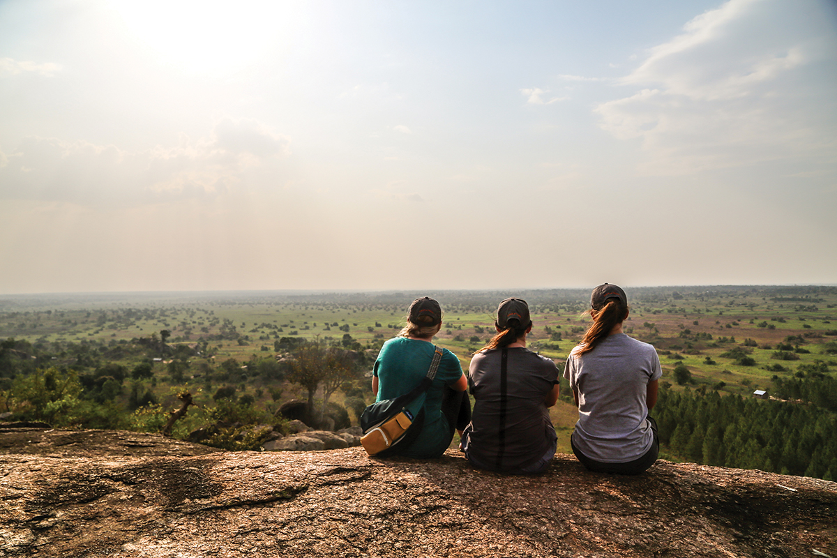 Three students sitting on rock at sunset