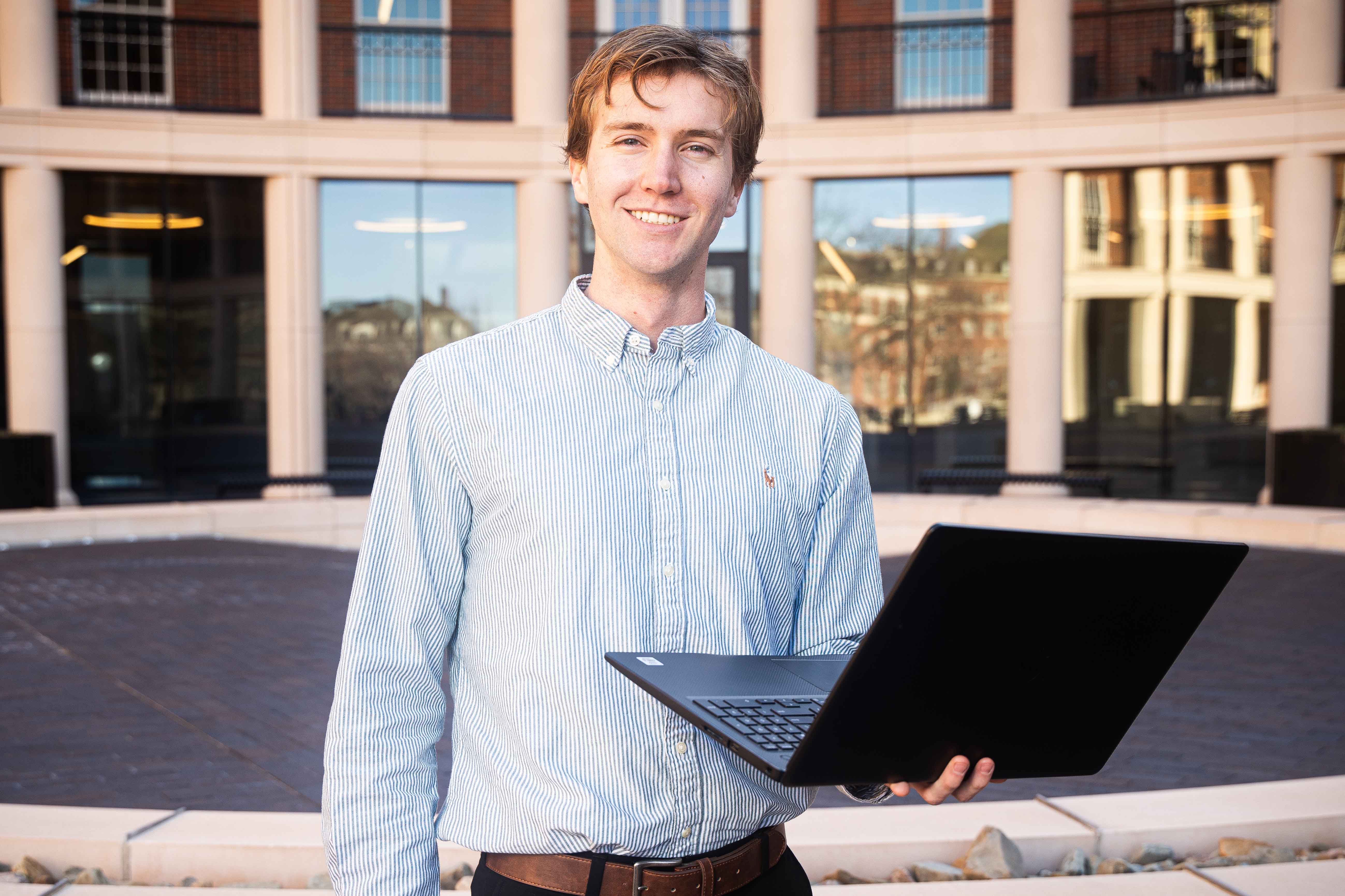 Student standing outside of the business building with a laptop.